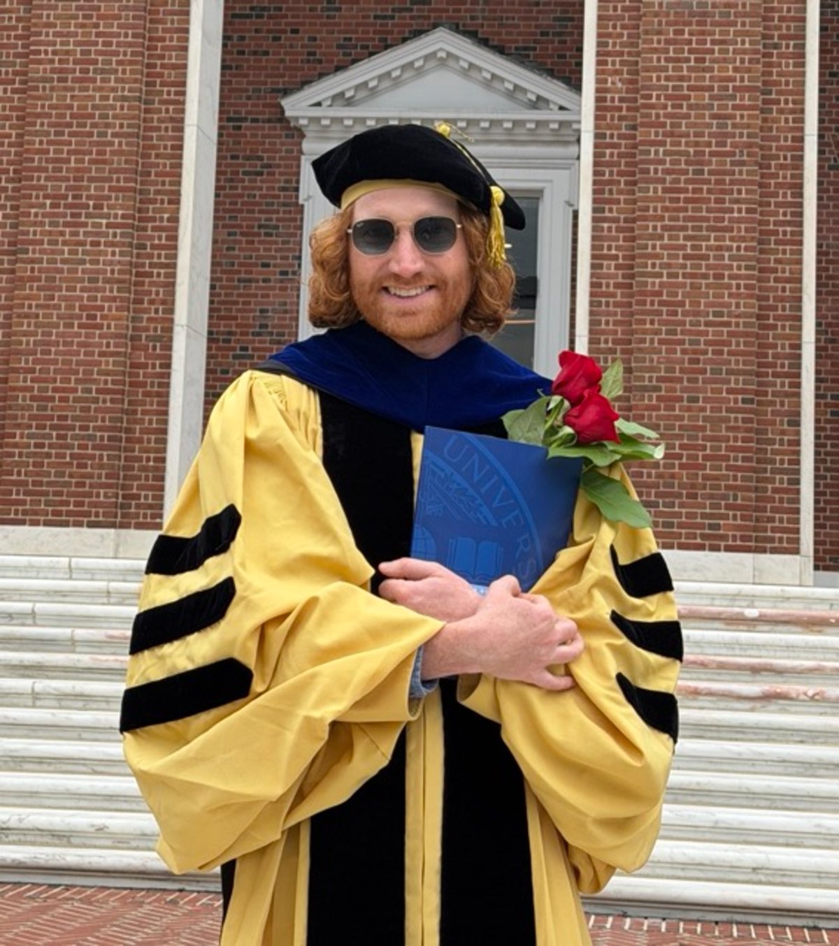 Dylan Gaeta in doctoral regalia outside Shriver Hall at Johns Hopkins University